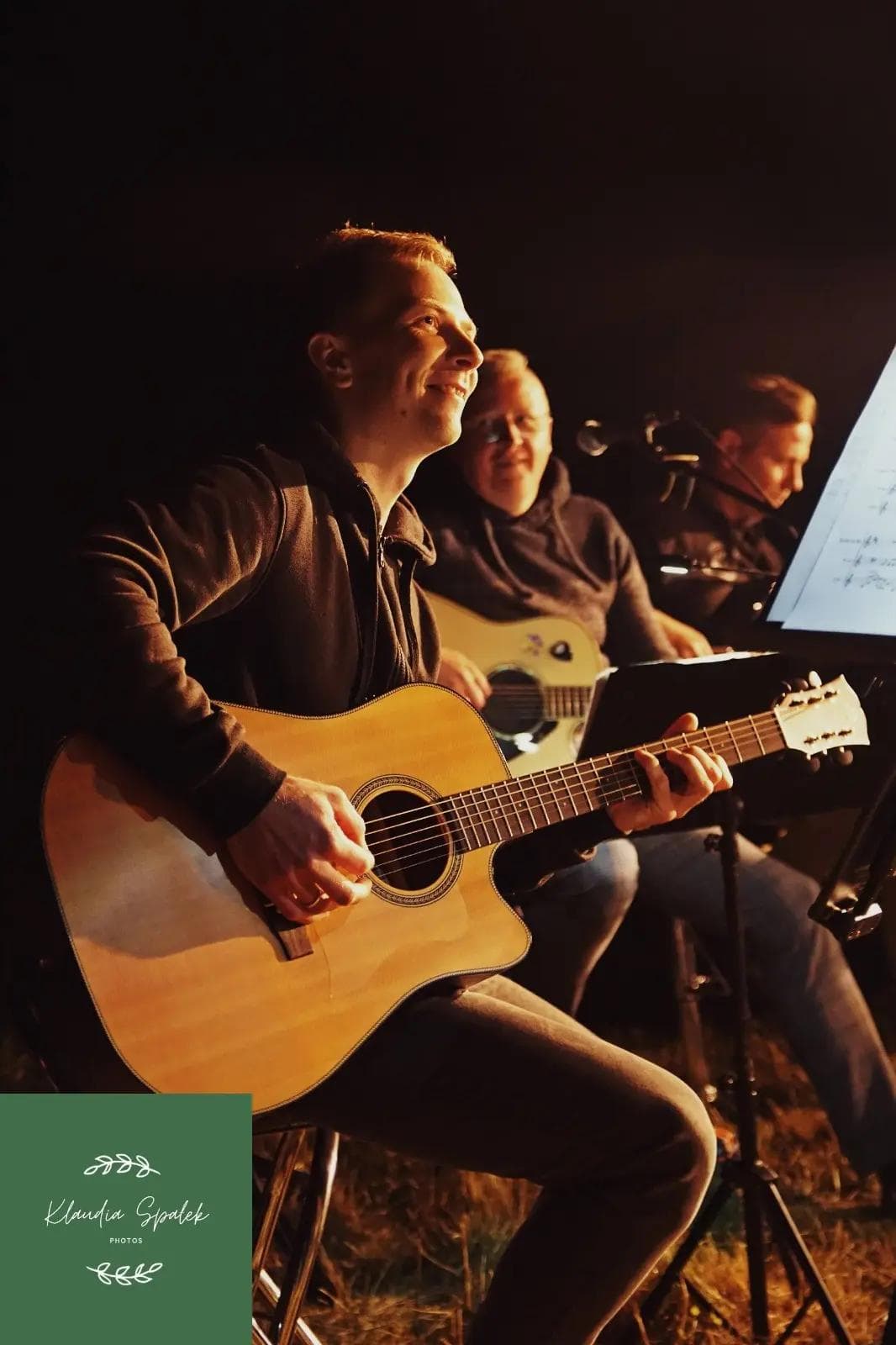 Trzech mężczyzn grających na gitarach w czasie wieczornego koncertu.